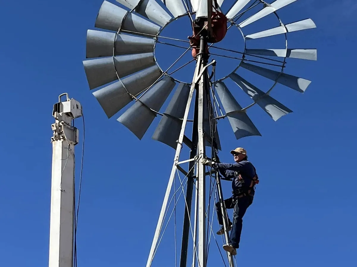 Technician harnessed high on a windmill tower with the pump hoist mast raised alongside