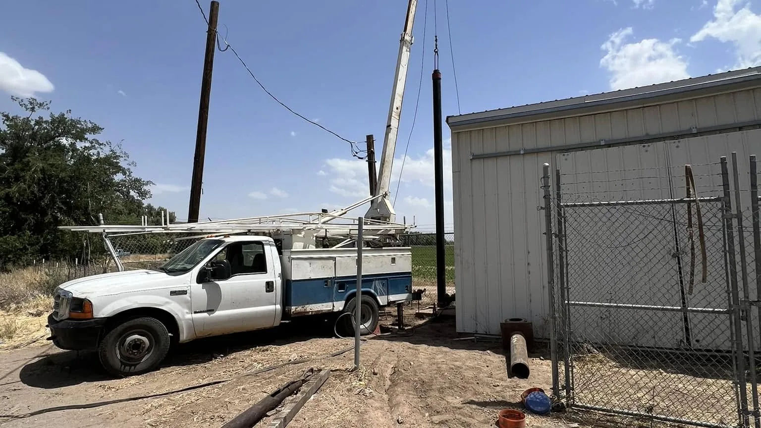 Service truck and pump hoist rig set up at a well beside a steel building