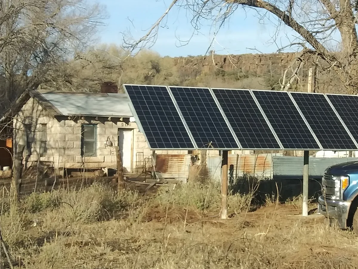 Ground-mounted solar array set beside an old stone ranch building to run the well