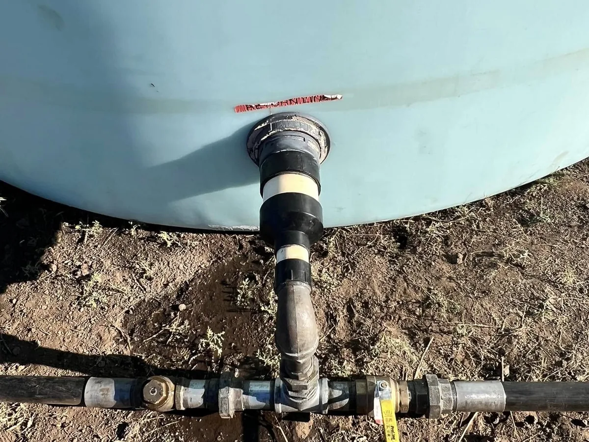 Outlet plumbing at the base of a water storage tank, tied into black poly pipeline