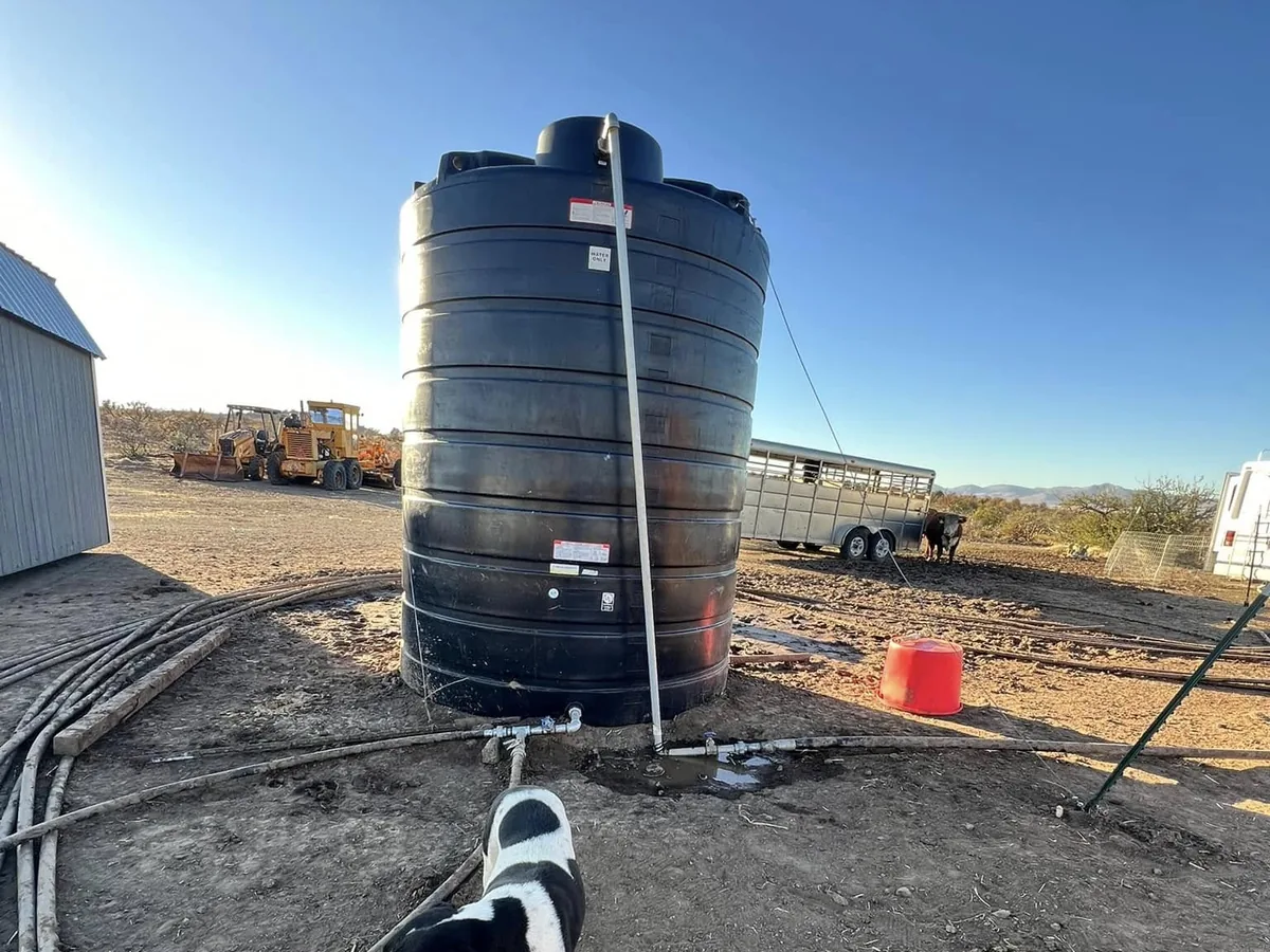 Black poly water storage tank plumbed on a ranch pad with buried supply line