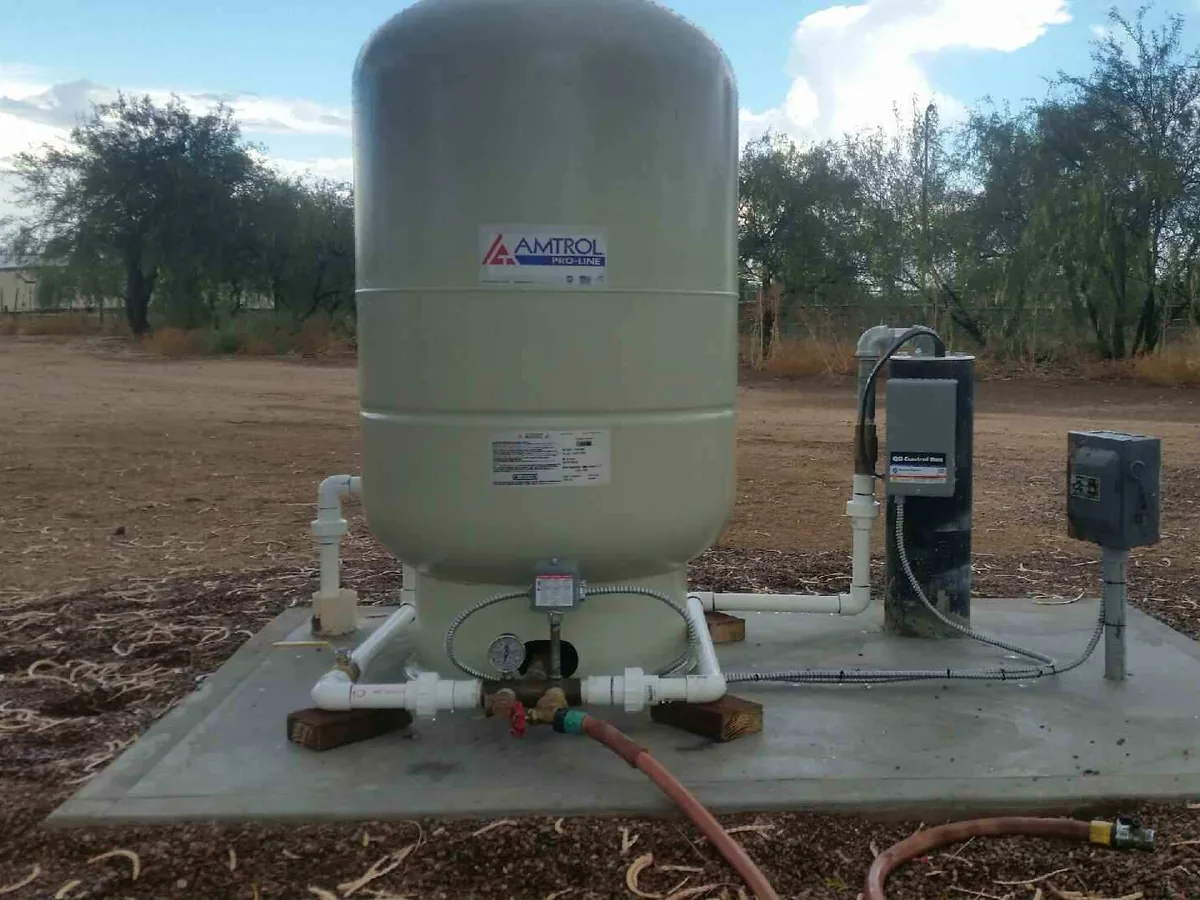 Pressure tank on a concrete pad beside a well with the pump control boxes on their post