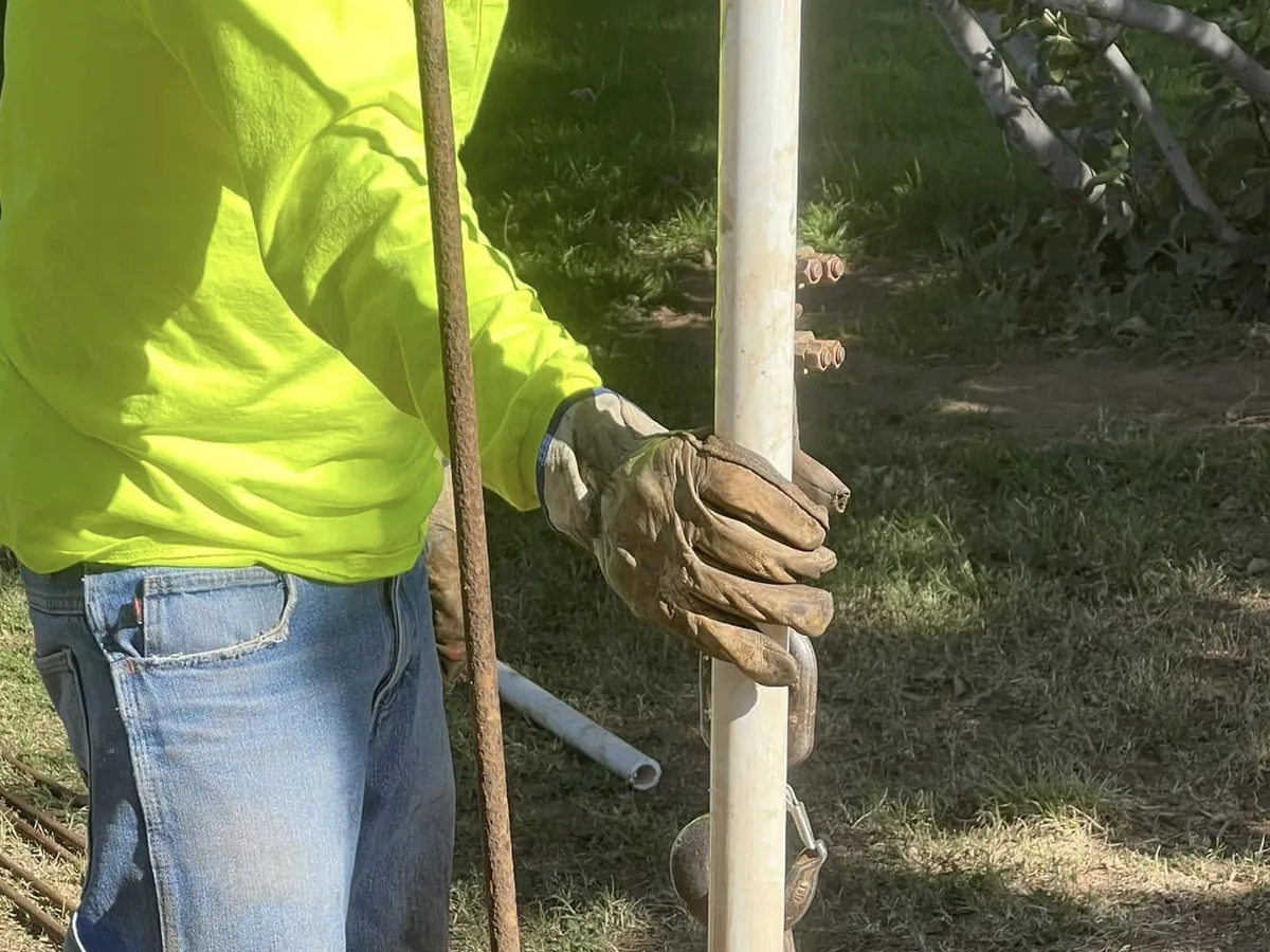 Gloved hands guiding the hoist line and pipe at an open wellhead