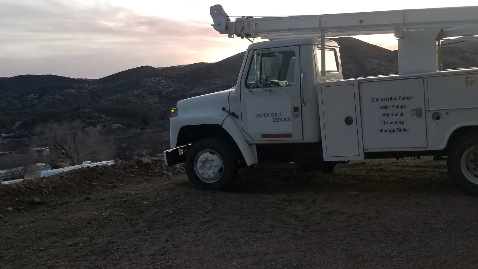 Well service truck with its folding derrick parked on a ridge at the end of the day